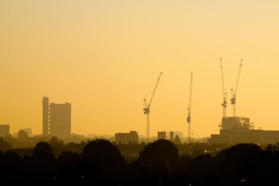 A tower block and cranes on an orange sky