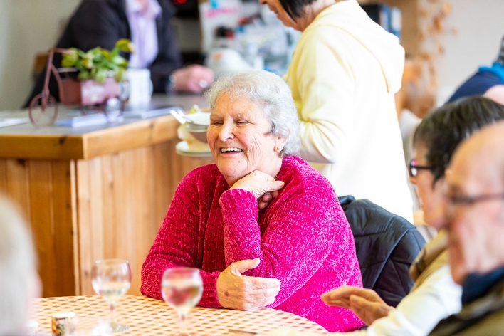 picture for projectStory: A woman in a pink jumper laughing while sitting at a table.