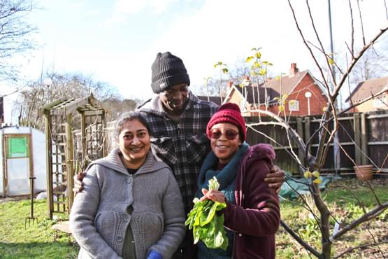 Three people stood in front of houses on an allotment