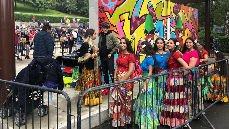 picture for projectStory: Women from the |Roma Community in Glasgow queueing for an outdoor gig at the Queen's Park bandstand in Govanhill. Behind them is a wall of colourful graffiti.